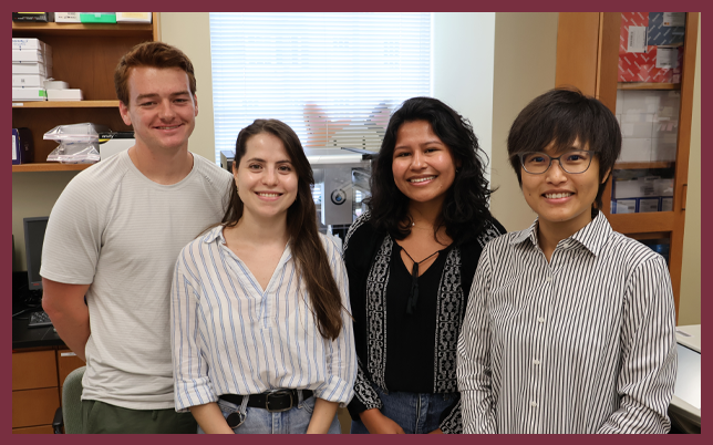 Four researchers—two men and two women—smiling while posing together in a brightly lit laboratory setting.