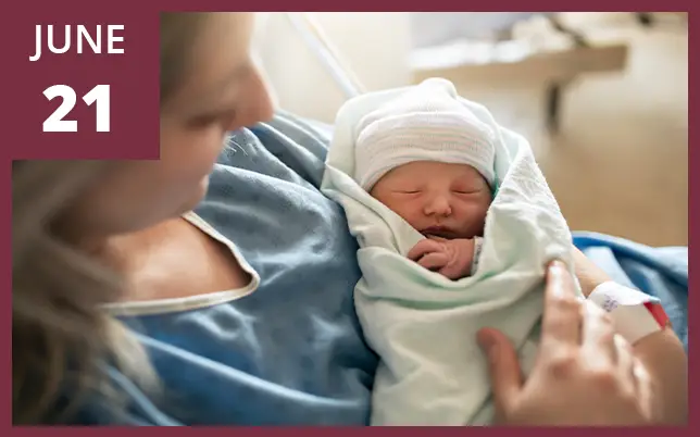 A close-up of a healthcare worker's hand in a blue surgical glove gently holding the foot of a newborn baby in a hospital setting. A maroon box in the top-left corner features the text 
