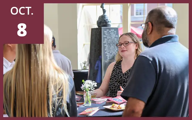 People networking at a table with drinks and programs, featuring 