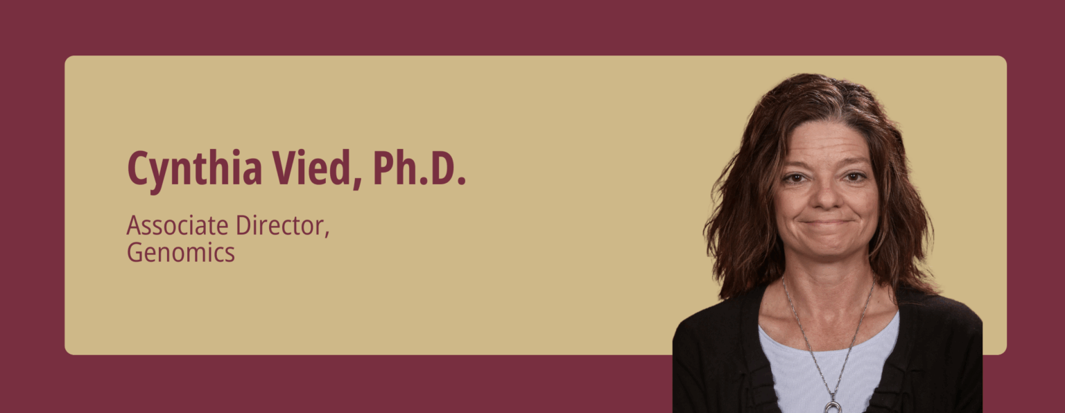 A professional headshot of Cynthia Vied, Ph.D., Associate Director, Genomics, presented on a tan text box overlaying a maroon background.