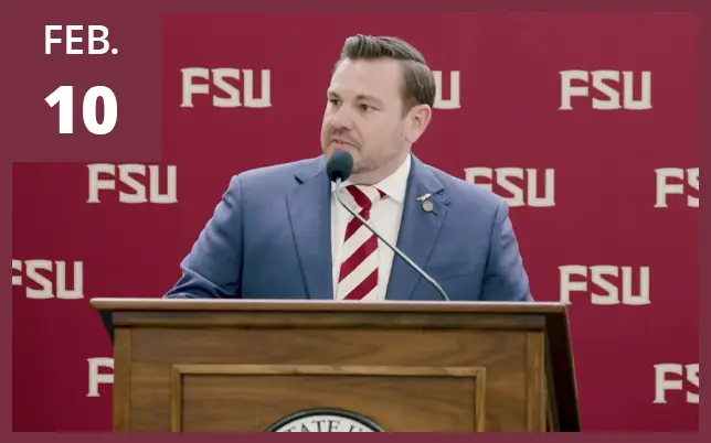 A man in a suit and striped tie speaks at a podium in front of an FSU backdrop next to a maroon box reading 
