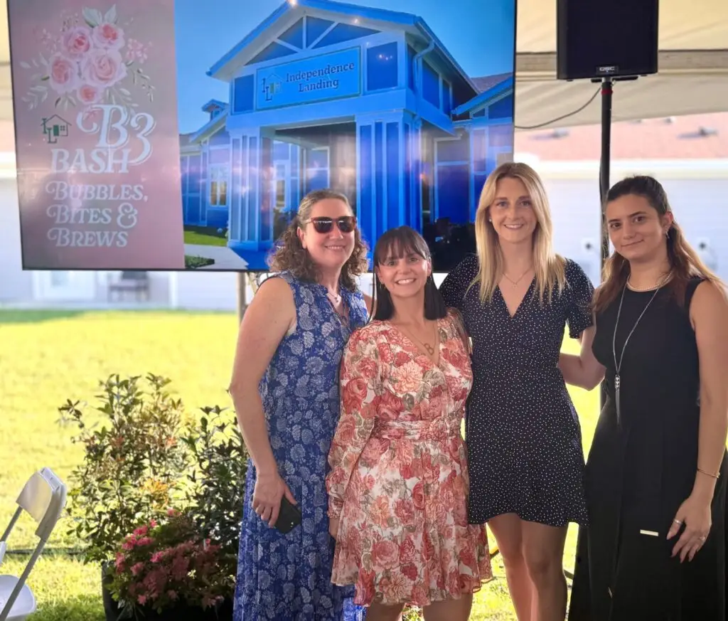 Four women pose for a photo in front of a digital display for the 