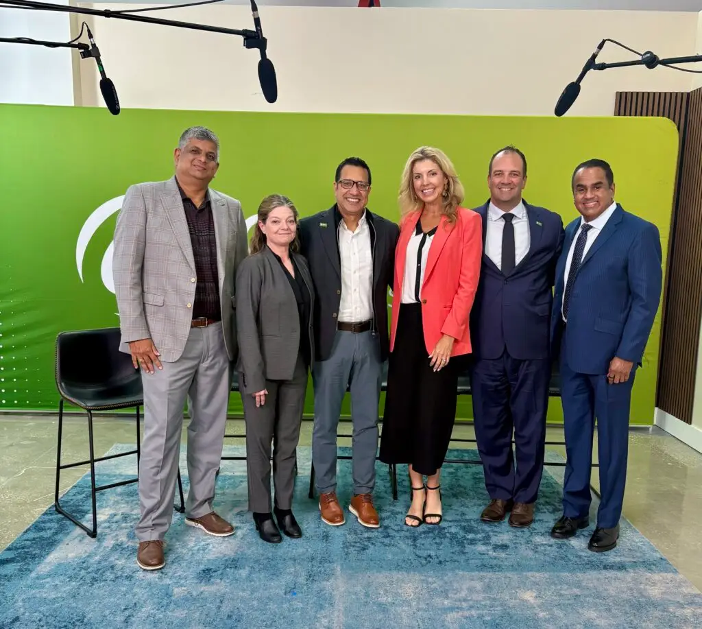 Six professionals stand in a row for a group photo in front of a green backdrop