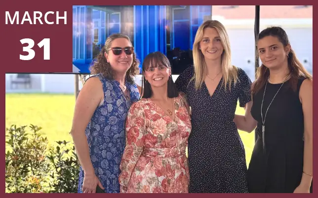 Four women pose together in front of a monitor with a garnet border in the upper-left corner featuring the text 