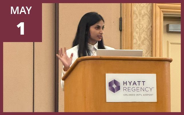 a woman speaking and gesturing with her hand at a wooden podium labeled "Hyatt Regency Orlando Int'l Airport," with a maroon box in the top-left corner displaying the text "MAY 1".